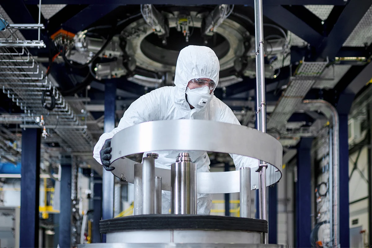 Technician in cleanroom suit operating industrial equipment in a high-tech manufacturing facility.