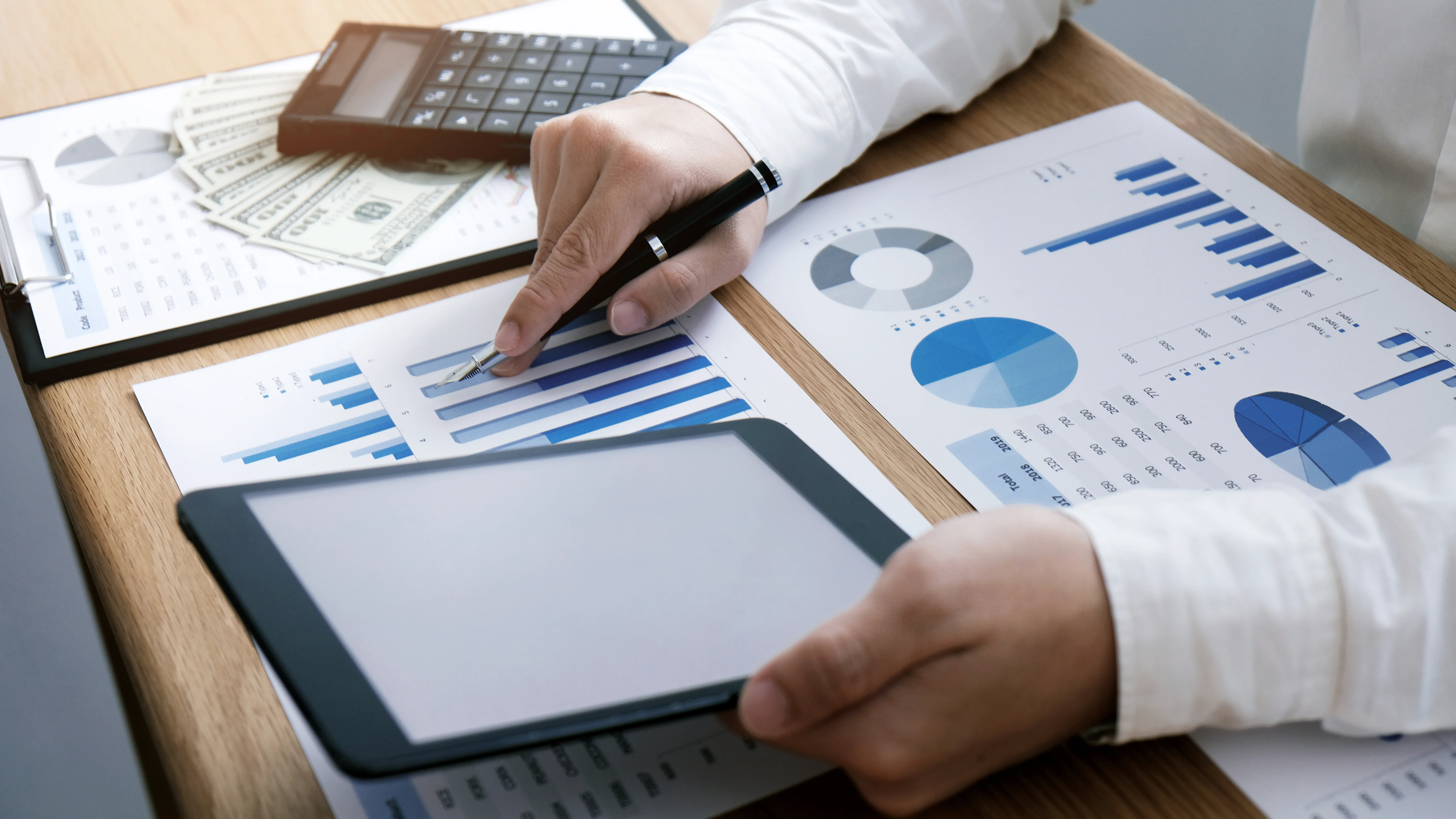 Hands reviewing financial charts with a tablet, calculator, and documents on a desk