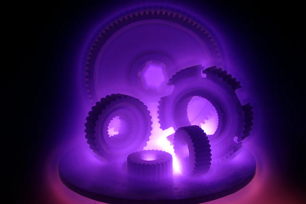 Purple plasma glow surrounding several circular metal parts inside a vacuum chamber.
