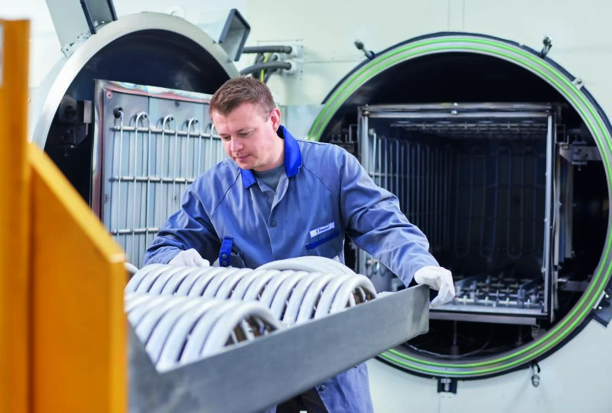 Worker loads a tray of metal components into the open chamber of a large high vacuum brazing furnace.
