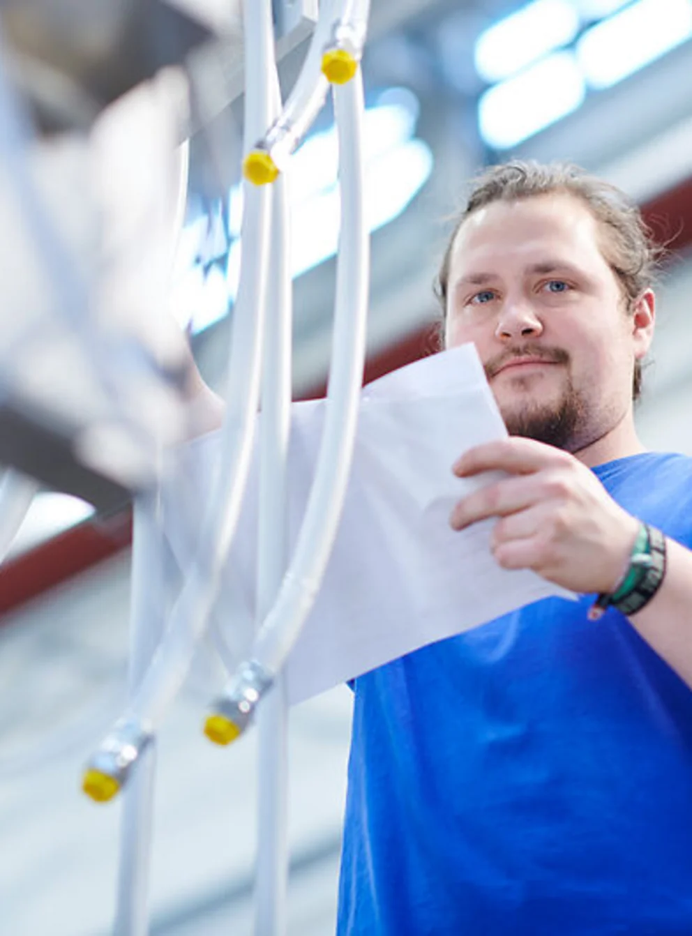 Worker reviews printed documents while inspecting equipment in a bright industrial facility.
