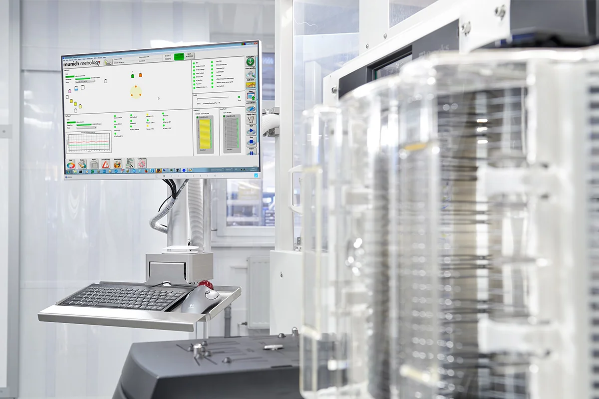 Cleanroom setup with monitor, keyboard, and wafer containers beside semiconductor equipment.