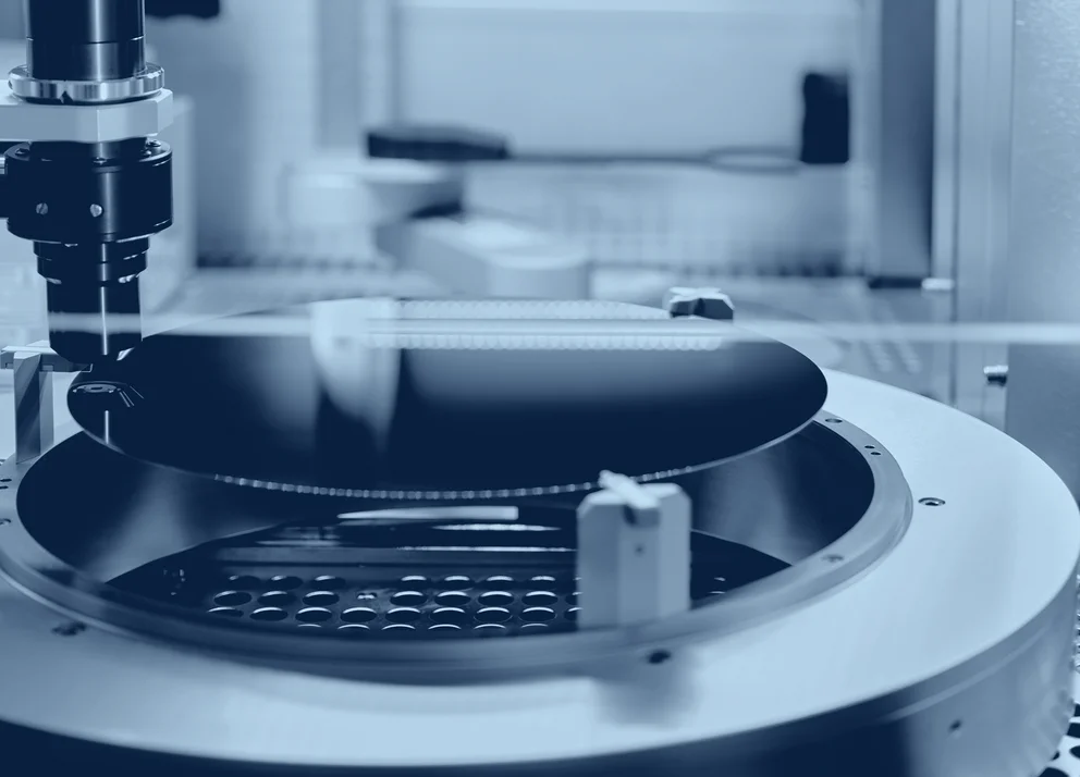 Close-up of a semiconductor wafer inside an automated processing or inspection station, with handling equipment positioned around the wafer