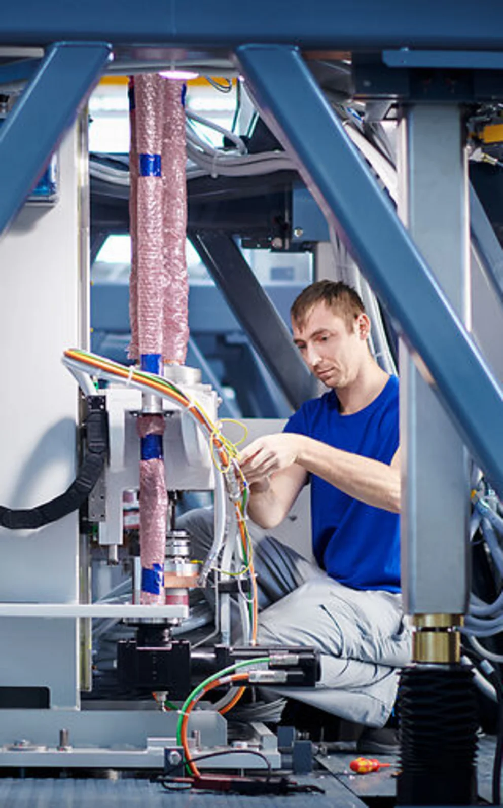 Worker adjusts components inside a large industrial machine frame with various cables and metal structures.
