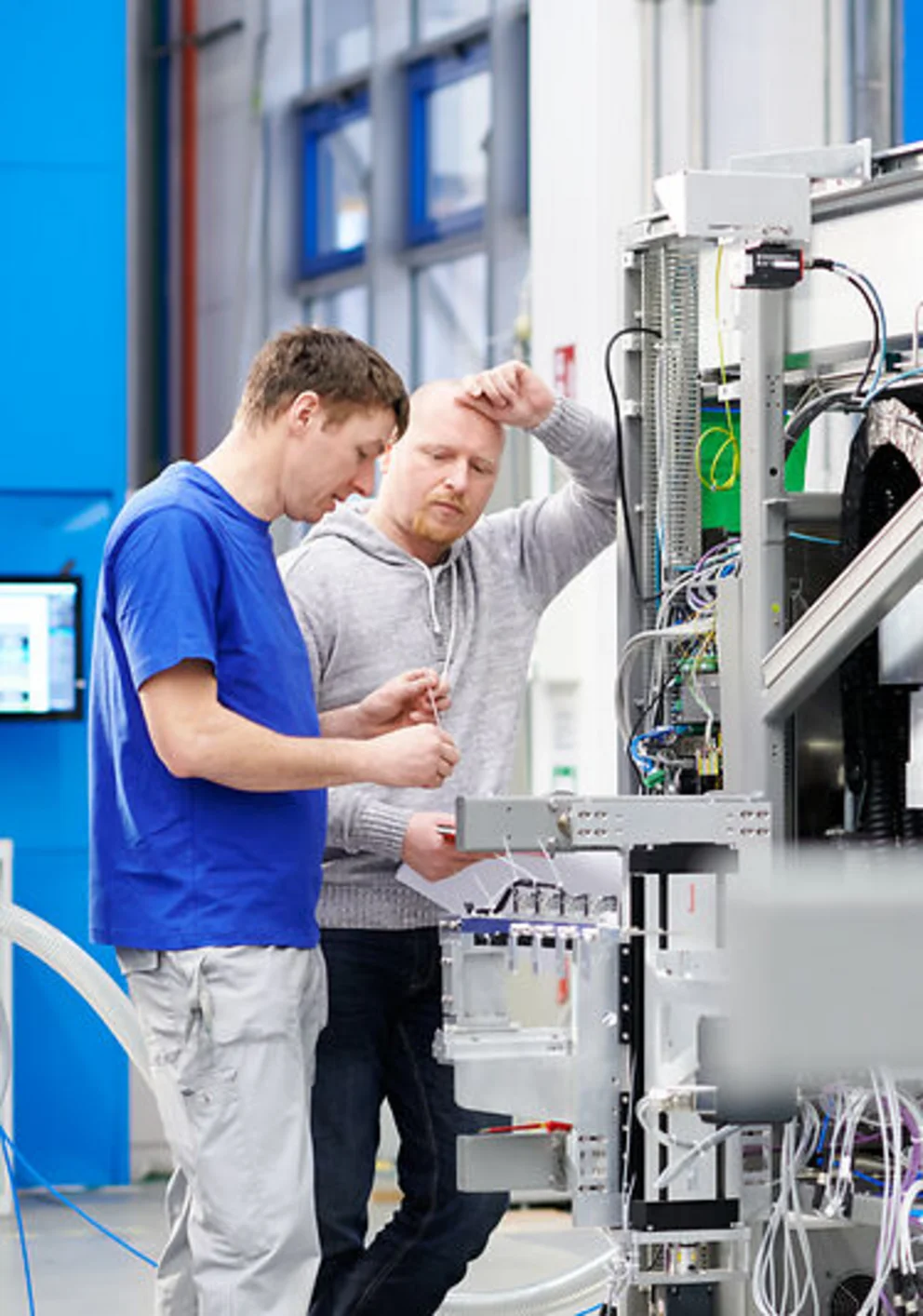 Two workers discuss technical details while inspecting an industrial machine in a bright production area.