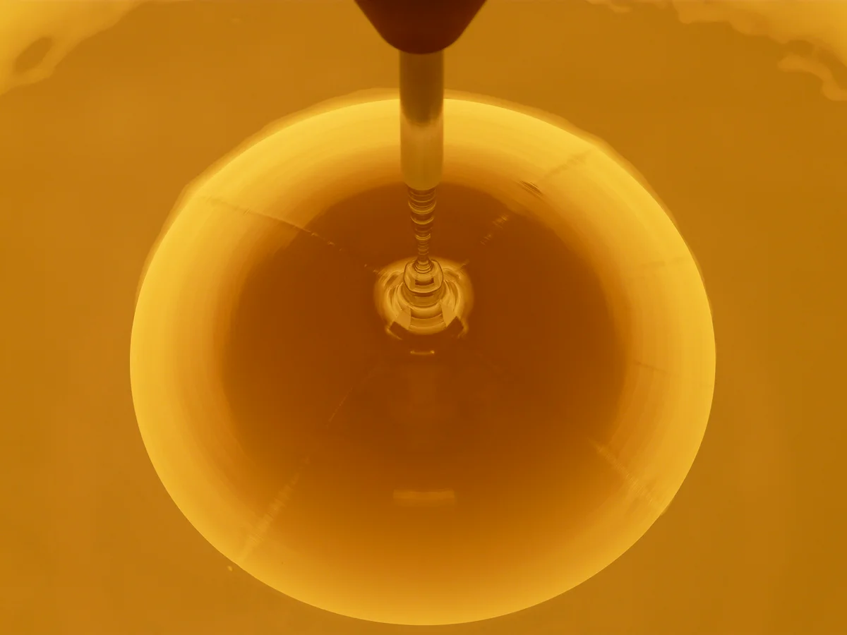 Circular melt in a crucible with a crystal growth seed rod centered above, viewed from above