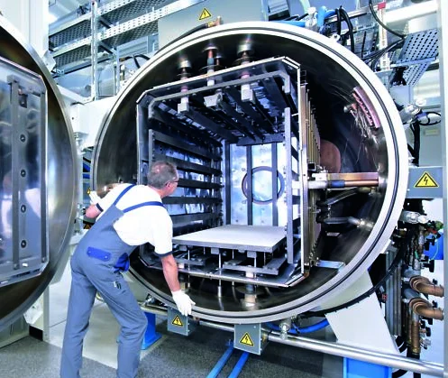 Worker loads components into the large open chamber of an vacuum brazing system inside a bright facility.