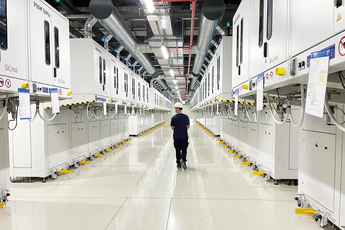 Person walking down a production hall lined with PVT SiCma crystal growth systems