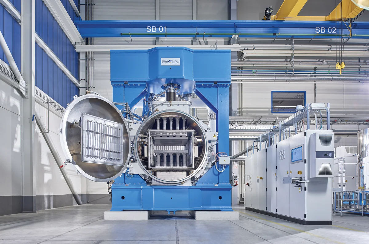 Two engineers standing beside a large blue industrial diffusion bonding system in a manufacturing facility.