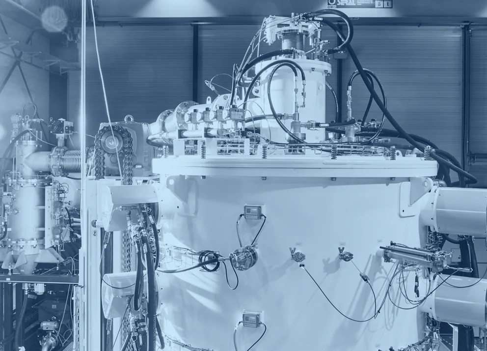 Large industrial processing chamber with connected piping, valves, and control components inside a production facility