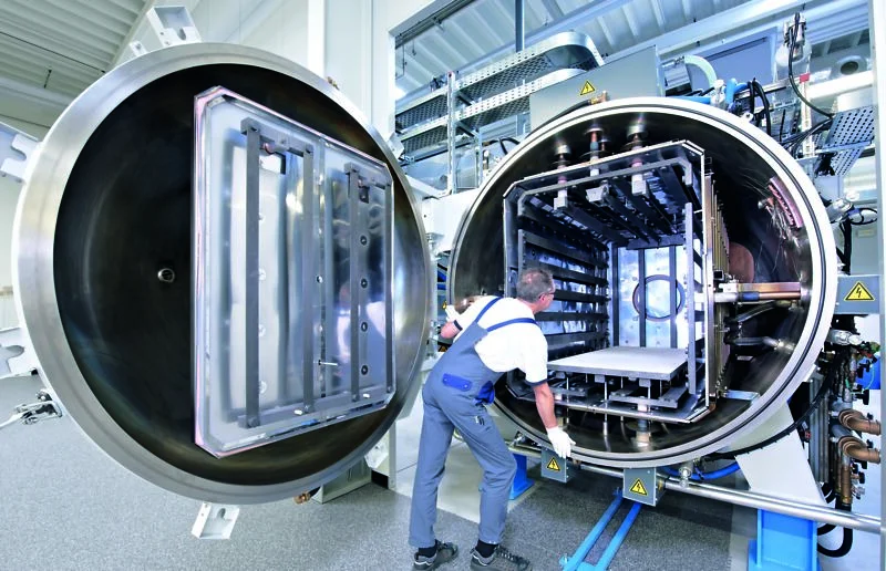 Worker loads components into the large open chamber of an vacuum brazing system inside a bright facility.