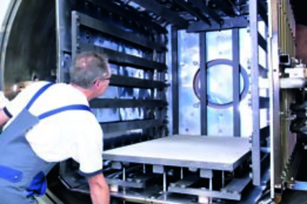 Worker loads components into the large open chamber of an vacuum brazing system inside a bright facility.