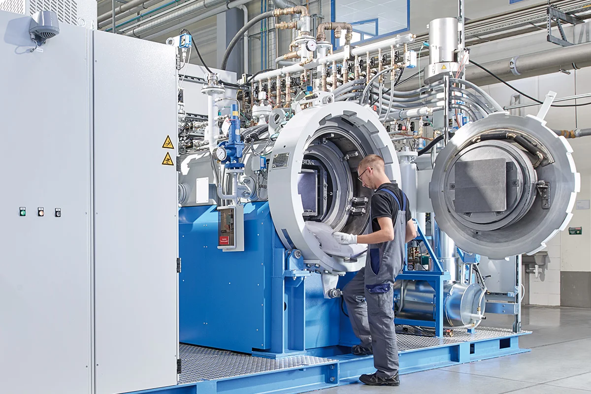 Technician operating a large industrial Sinter-HIP furnace system in a manufacturing facility.