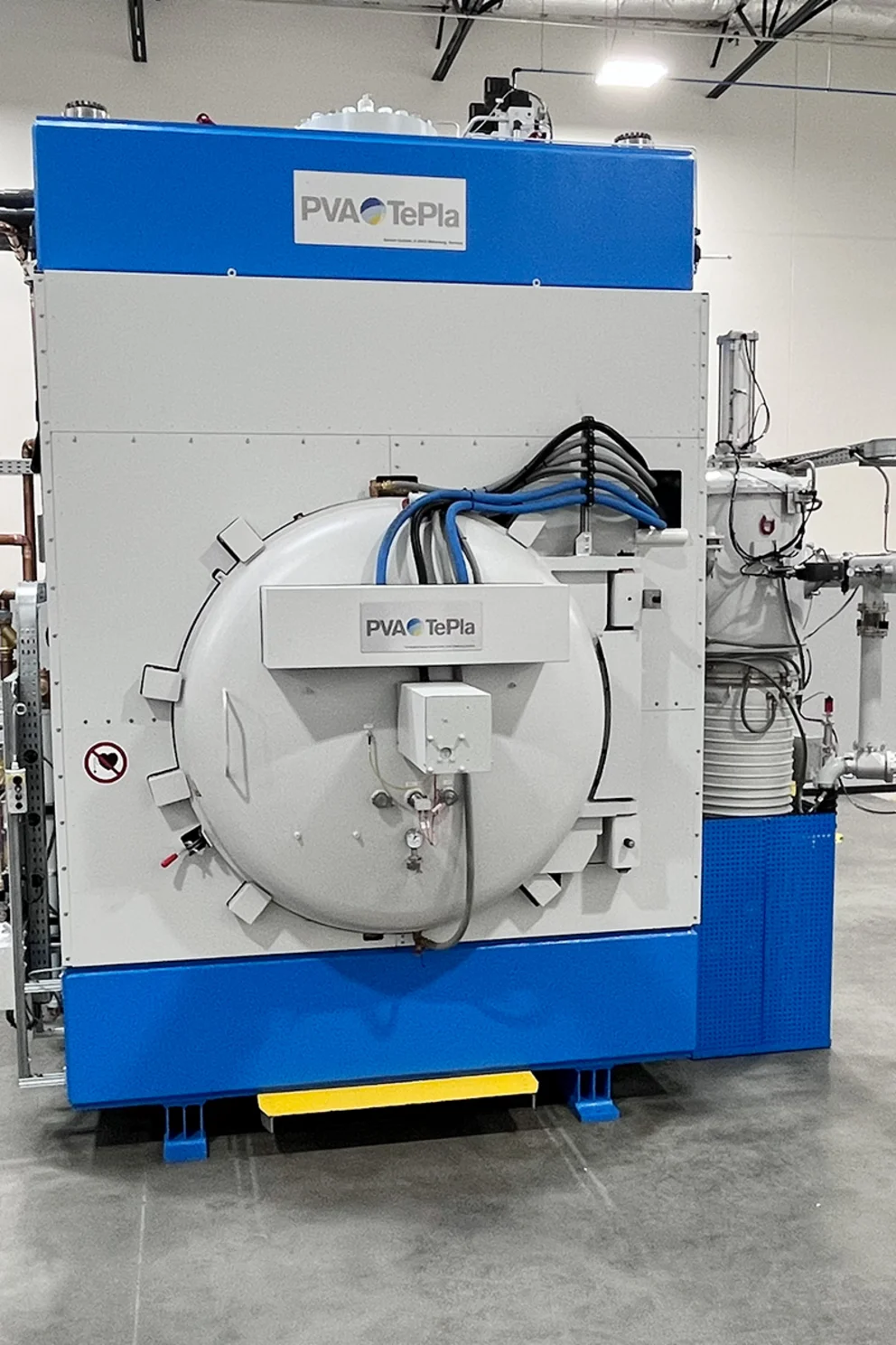 Compact industrial diffusion bonding system with circular vacuum chamber door in a manufacturing facility.