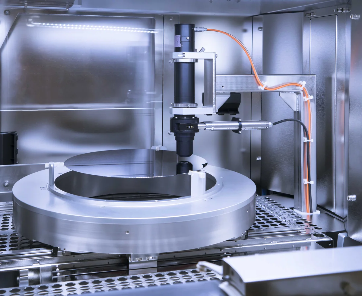Internal view of a PVA TePla SIRD system showing a wafer mounted on a rotating stage with precision inspection sensors and robotic components inside the stainless-steel chamber.