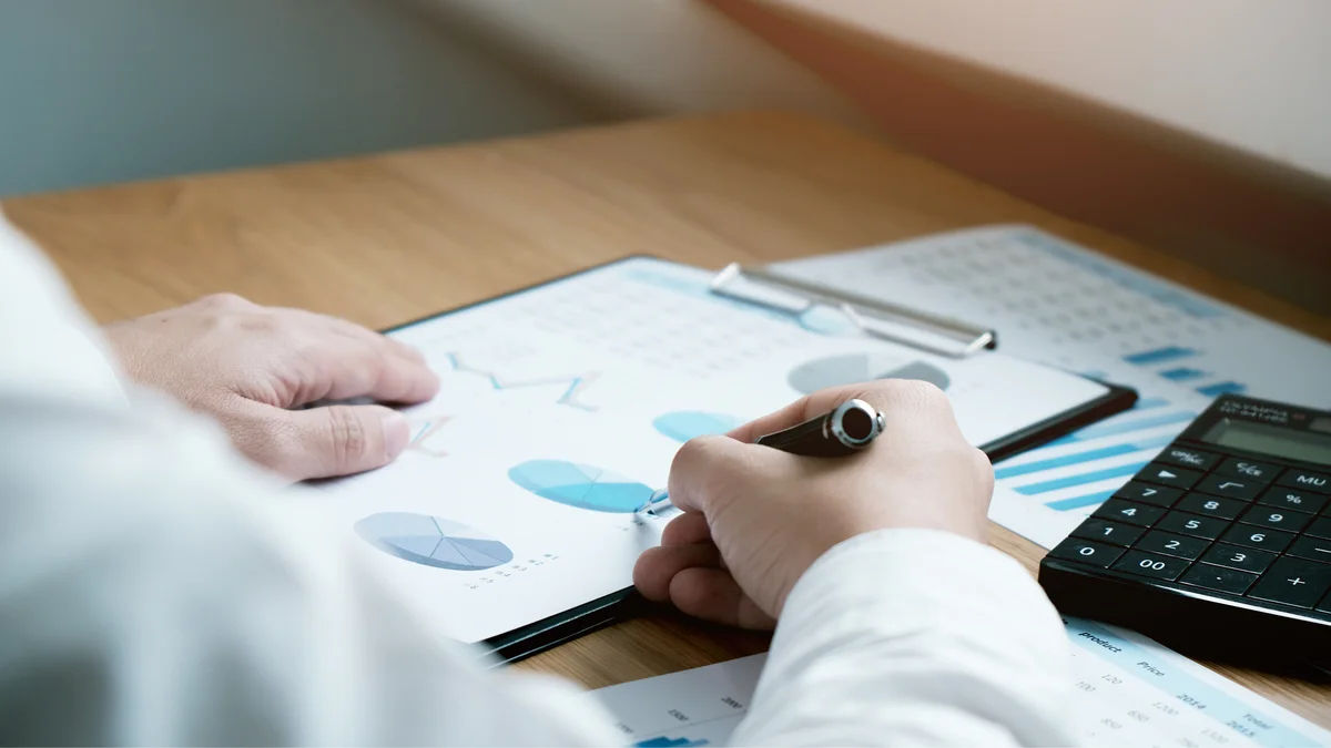 Hand writing notes on financial charts at a desk